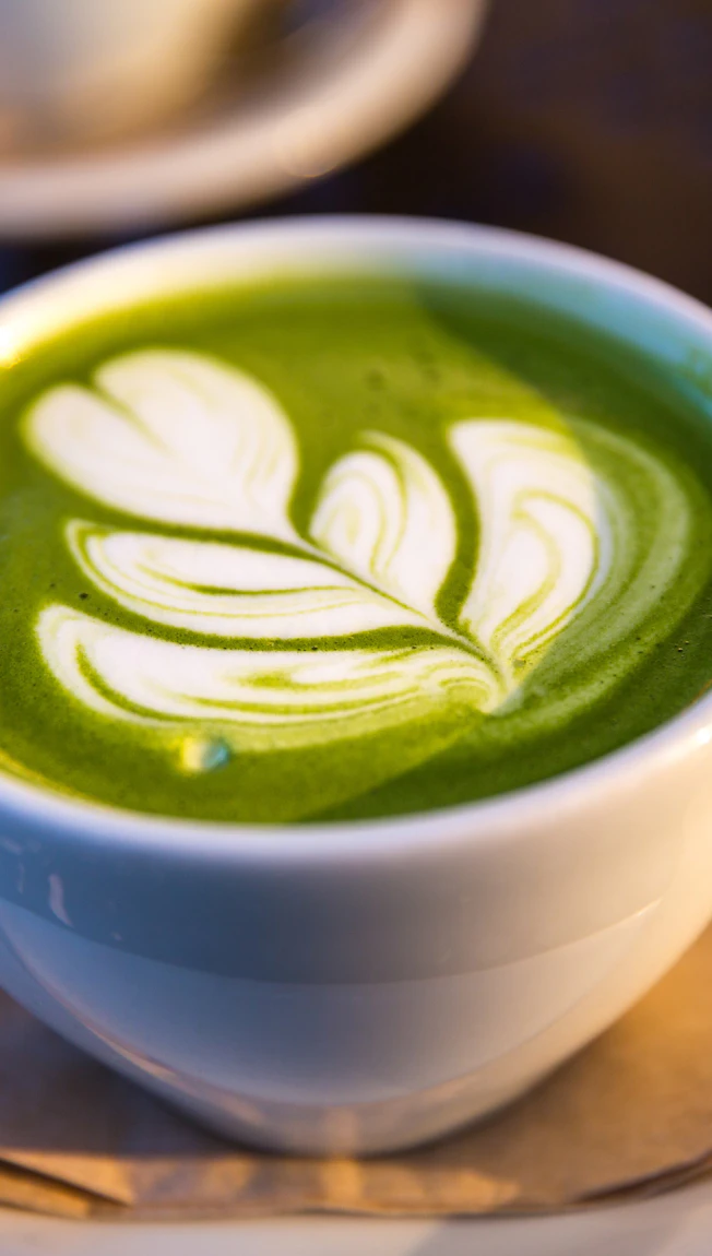 A matcha latte with leaf latte art on the counter
