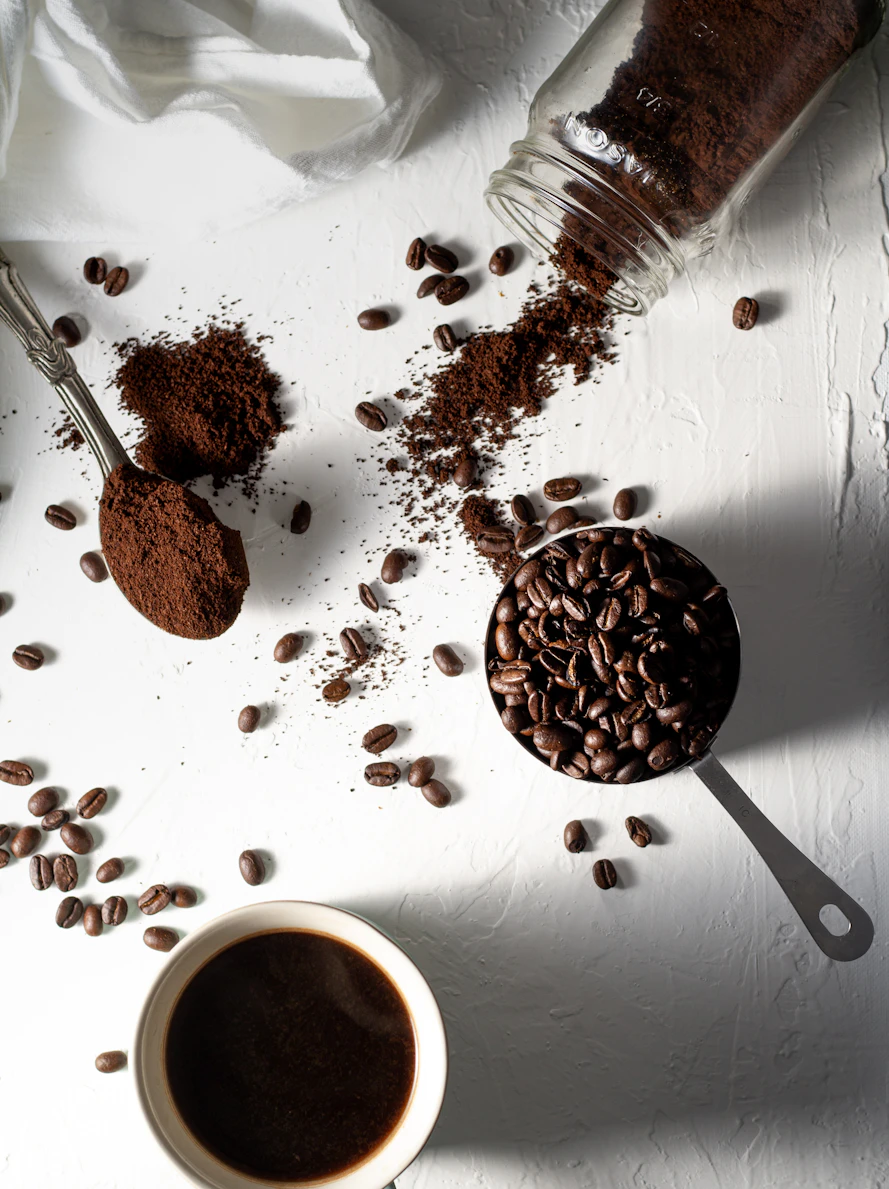 Coffee beans, fresh grounds and a cup of drip coffee on a white table