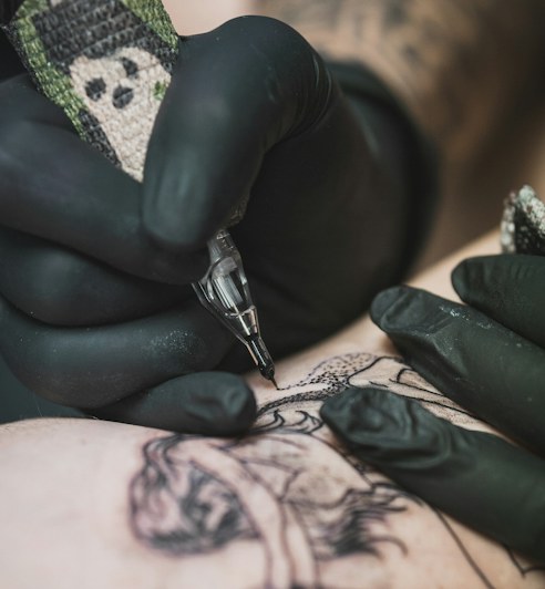 A raven with spread wings across a chest above hanging geometric ornaments, tattooed by Wren.