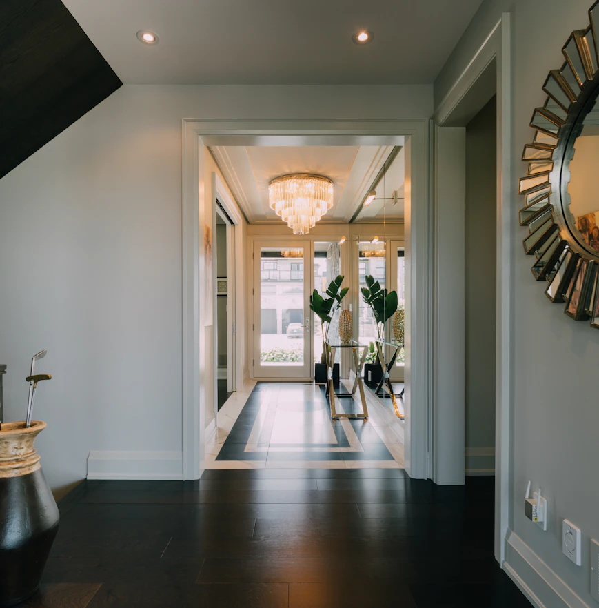 A long entrance hallway with a chandelier and a sunburst mirror.