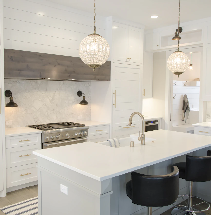 A white shaker kitchen with a marble island and pendant lights.