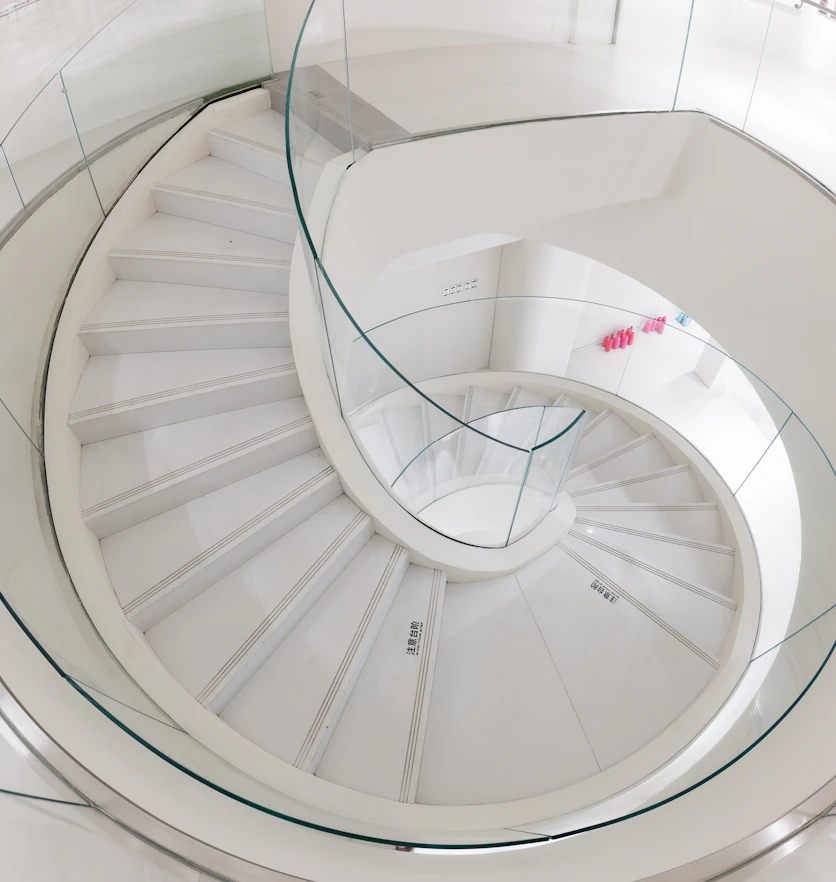 A white spiral staircase with a curved glass balustrade.