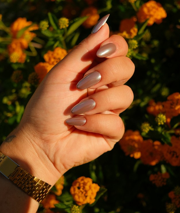 Almond nails finished in rose-gold chrome held against orange blooms