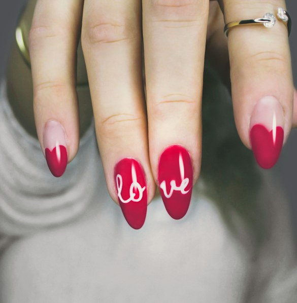 Almond nails in deep red with hand-lettered white script on two nails