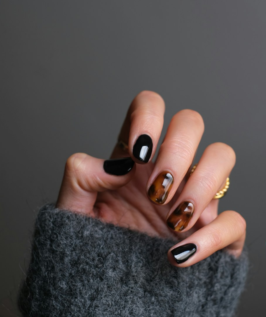 Almond nails in glossy black and tortoiseshell against a grey knit