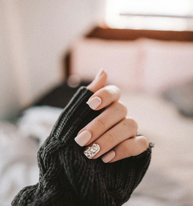Short nude nails with a single glitter accent nail against a dark knit