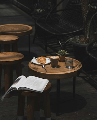 Low wooden stools and a small round table with an open book and a coffee, in the dark corner