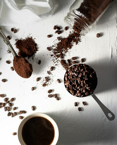 Ground coffee, whole beans and a small black coffee laid out on a white table