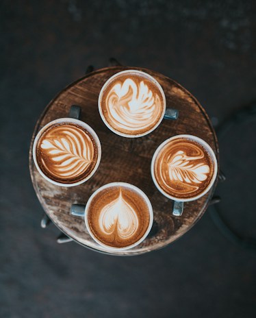 Four lattes with hearts and rosettas in the foam, seen from above on a round wooden table