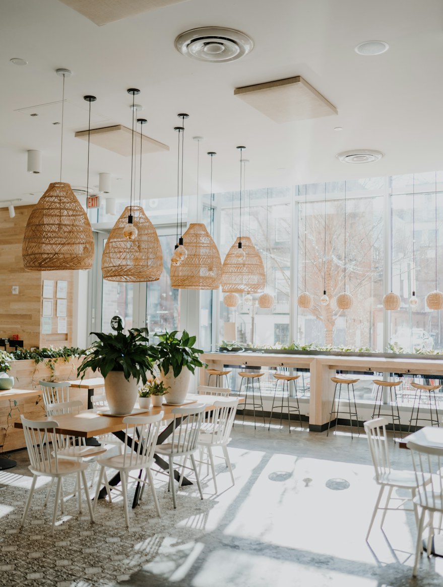 The bright room: white bentwood chairs, rattan pendant lamps in a row, potted plants, and the tall windows onto the street