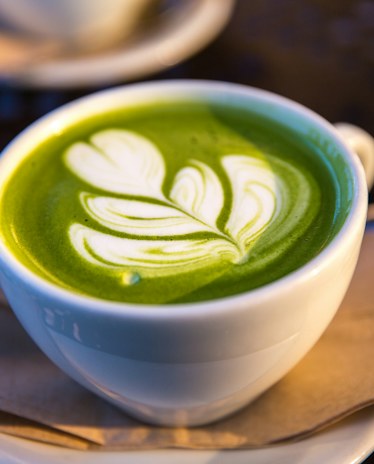 A matcha latte in a white cup with a leaf poured in the foam