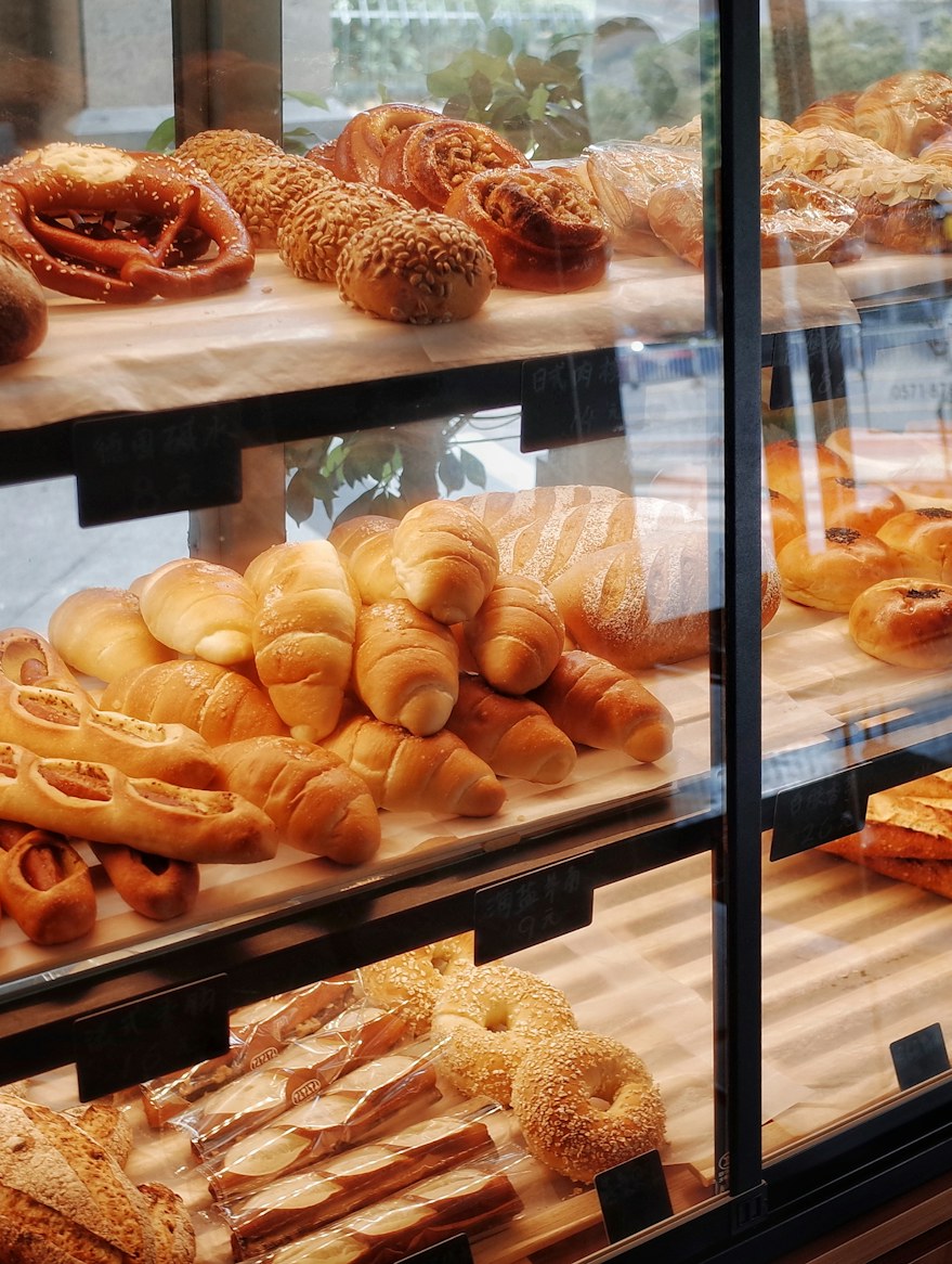 The glass pastry case: seeded rolls on the top shelf, croissants in the middle, and a tray of twisted pastries below, on brown paper