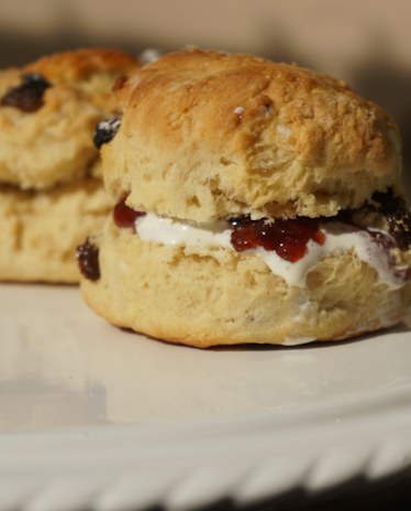 A scone split and filled with cream and jam, on a white plate by the window