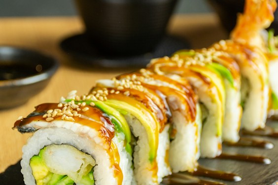 Rolls topped with salmon and avocado on a dark plate, on the marble counter.