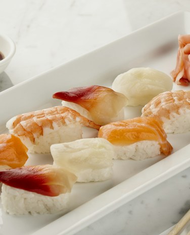 Six pieces of torched aburi sushi on a white plate with lemon and wasabi.