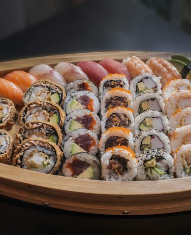 A round wooden board of rolls, nigiri and sashimi, seen from above.