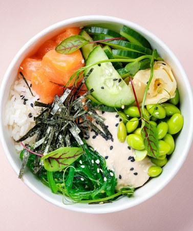 A poke bowl of cubed salmon with seaweed salad, tomato and red cabbage.