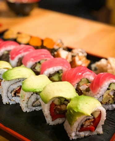 A dragon roll on a slate board, topped with sliced avocado and herbs.
