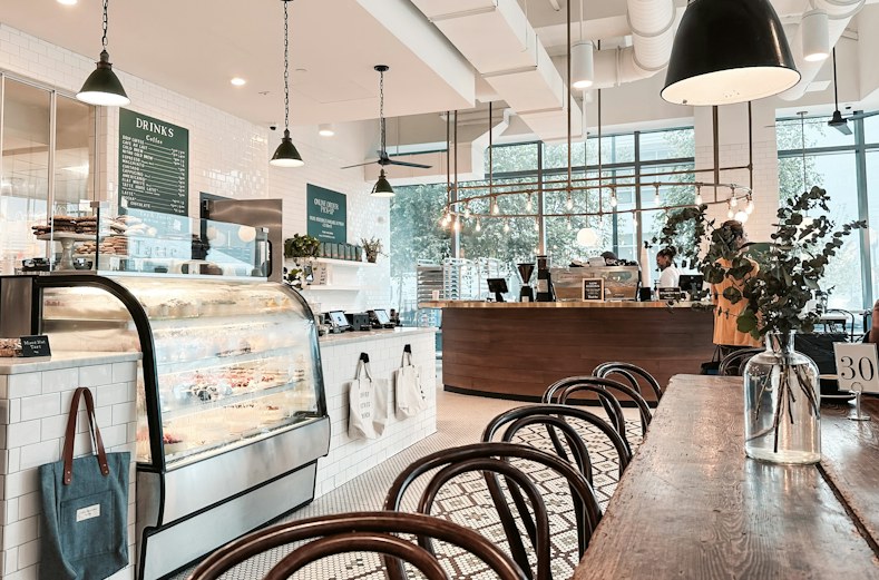 The bakery interior: oak counter, white brick, globe pendants, sheer curtains and a dried-flower installation