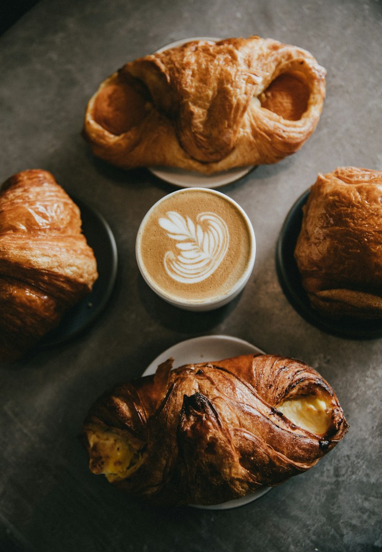 Croissants around a flat white on a dark table