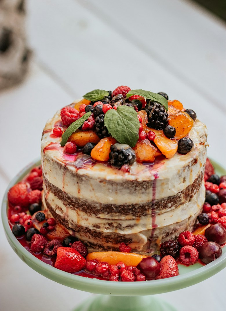 A naked layer cake crowned with berries and peaches, on a cake stand