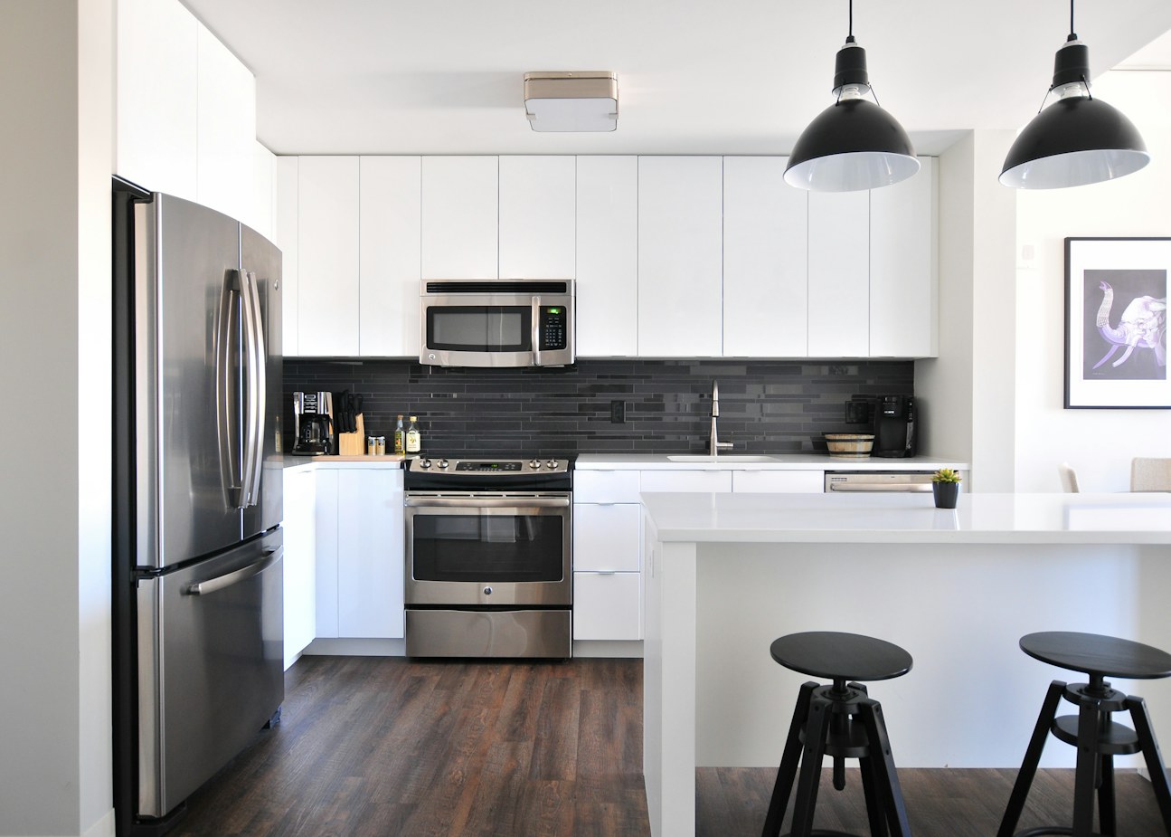 White galley kitchen with black tile backsplash, stainless range and dark wood floor
