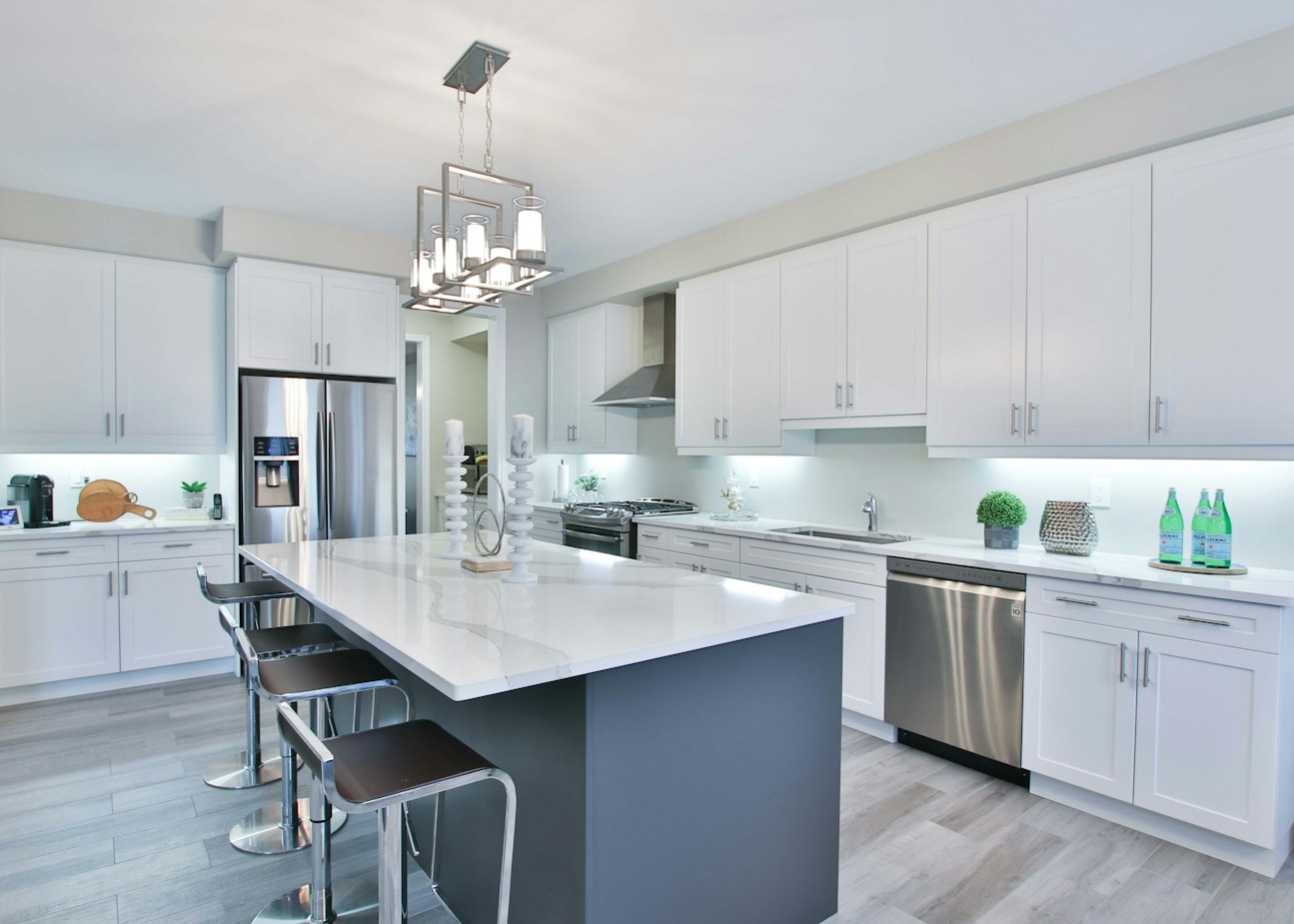 Condo kitchen with a quartz island, stainless appliance run, white shaker cabinetry and a pendant cluster